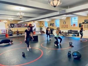 People training with kettlebells and bodyweight exercises in martial arts gym.