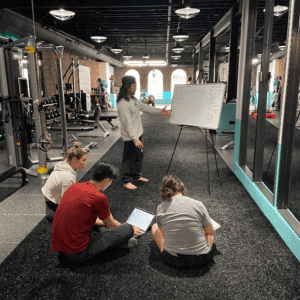 Group of people in boxing gym attending a training session with instructor and whiteboard.