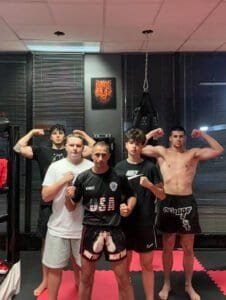 Group of fighters in Muay Thai gym flexing muscles after training.