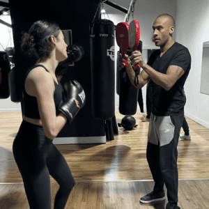 Female boxer practicing punches with trainer at NYC boxing gym.