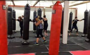 People practicing boxing techniques with punching bags in a gym.
