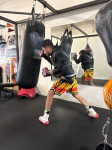 Young boxer practicing punches on a heavy bag in gym.