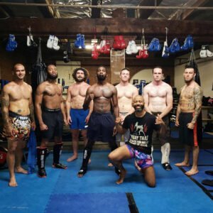 Group of diverse fighters and trainer at Low Kick Camp gym.