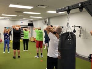 Group of Parkinson's patients doing stretching exercises in boxing gym.