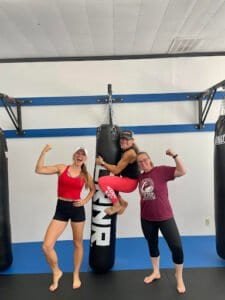 Group of women and man flexing muscles in boxing gym with punching bags.
