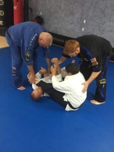 Two instructors assist a student during Brazilian Jiu-Jitsu practice at Elite M.M.A. Center.