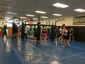 Group of people practicing martial arts in a gym with punching bags.