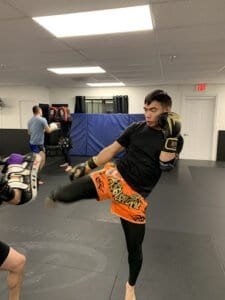Young man practicing kickboxing in a gym with focus mitts and training equipment.