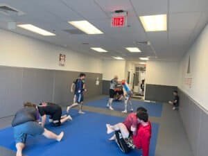 Students practicing Brazilian Jiu Jitsu techniques in a martial arts training room.