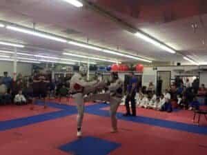 Kids practicing martial arts sparring in a gym with spectators.