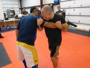 Two men practicing Krav Maga self-defense techniques in a gym.