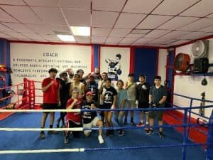Group of boxers and trainers in boxing gym with boxing ring and motivational wall.