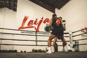 Boxers practicing sparring in the Leija Boxing gym with focus mitts and boxing ring.