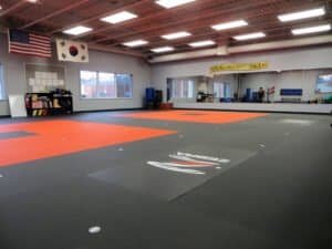 Indoor martial arts training gym with mats, flags, and training equipment.