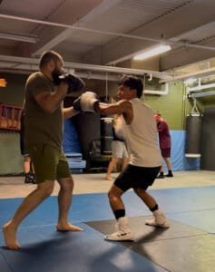 Young boxer practicing punches with trainer in gym.