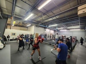 Boxers training in a boxing gym with a ring and trainers present.