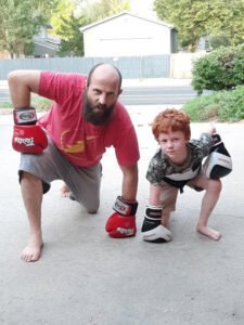 Adult coach and young boy practicing boxing stance outdoors.