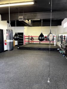 Indoor boxing gym with punching bags and boxing ring for training.
