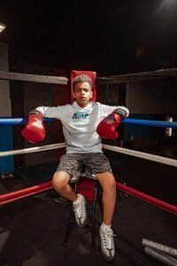 Young boy with boxing gloves sitting in boxing ring at Kingdom Boxing & Fitness Center.
