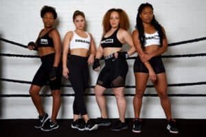 Four women boxers in athletic gear in boxing ring at BOOMBOX Boxing Club.