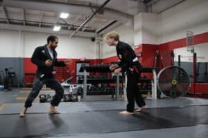 Two practitioners sparring in Brazilian Jiu-Jitsu training at gym.
