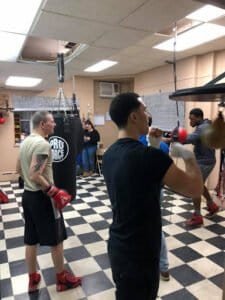 Young men practicing boxing techniques in gym with punching bags.