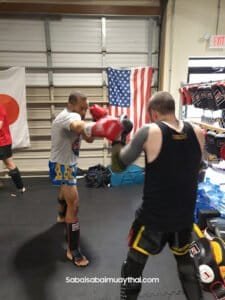 Two fighters practicing Muay Thai with focus mitts in gym.