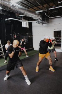 Group of people practicing boxing in a gym with boxing gloves and pads.