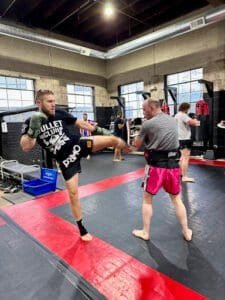 Muay Thai fighters practicing kicks and punches in gym training session.