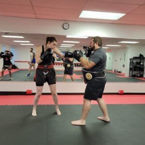 Female and male fighters practicing Muay Thai boxing techniques in gym.