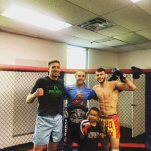 Group of fighters in MMA gym with cage and training gear.