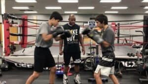 Two young boxers sparring with coach in a boxing gym.