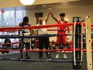 Young male boxer wins match, raising hand in victory at boxing gym.