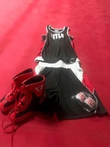 Boxing shoes, gloves, and athletic wear on a red gym floor.