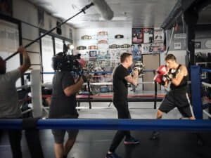 Boxers training in ring at Daruma Combat Sports gym with camera crew.