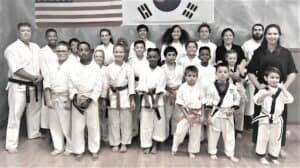 Group of children and instructors in martial arts uniforms in dojo.
