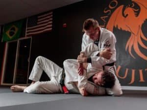 Two practitioners practicing Brazilian Jiu-Jitsu in a gym with flags and logo.