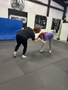 Two women practicing Brazilian Jiu-Jitsu techniques in a training gym.