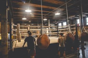Indoor boxing gym with heavy bags and a boxing ring for training and sparring.