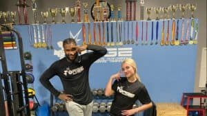 Two athletes posing with medals and trophies in a boxing gym.