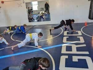 Children practicing martial arts drills in a gym with instructor supervision.