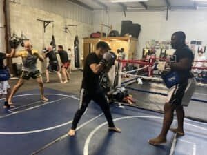 Boxers training in a Muay Thai gym with focus mitts and punching bags.
