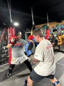 Boxers practicing sparring in a gym with punching bags and graffiti wall.