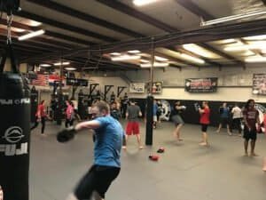 People training in a boxing gym with punching bags and trainers.