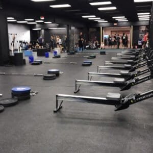 Indoor CrossFit gym with rowing machines and people working out.