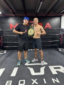 Boxing champion holding championship belt with coach in boxing gym.