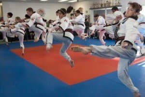 Kids practicing martial arts kicks in a dojo with instructor supervision.