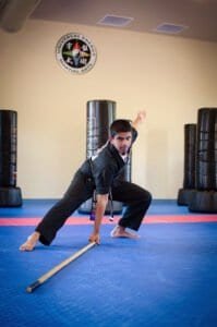 Martial arts student practicing staff techniques in training dojo.