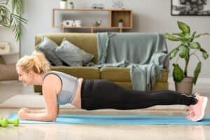 Woman doing plank exercise on yoga mat at home for fitness.