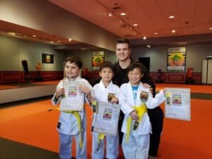 Young students in taekwondo uniforms holding certificates in martial arts class.